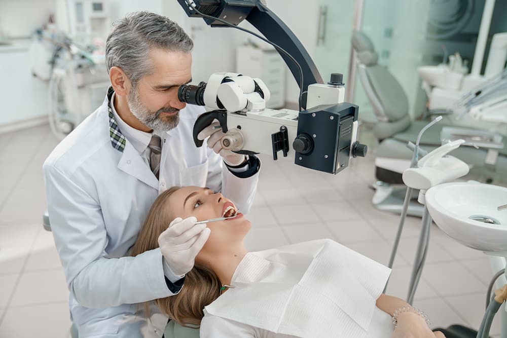 doctor looking through dental microscope at teeth CQTD9N6 1