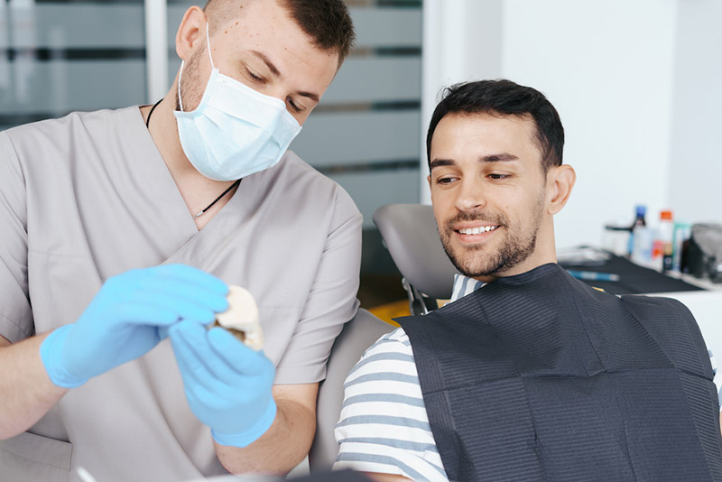 male-dentist-showing-patient-the-artificial-dentur
